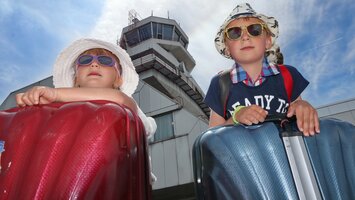 Geschwisterpaar mit Koffer, Sonnenbrille und Hut vor Tower | © Linz Airport