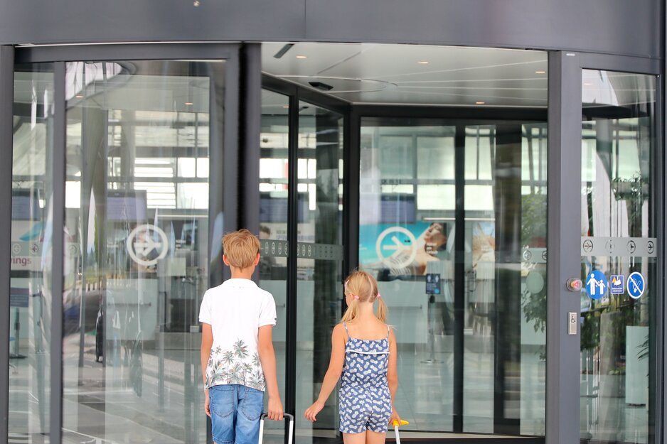 Geschwisterpaar mit bunten Rollkoffern beim Betreten der Abflughalle | © Linz Airport