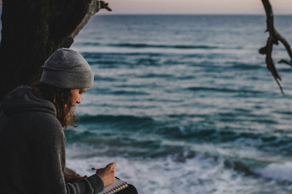 Junge Frau schreibt am Strand in ein Tagebuch | © Unsplash