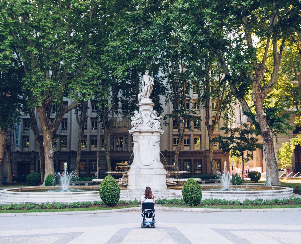 Frau im Rollstuhl vor Brunnen mit Statue | © Carlos Navas Unsplash