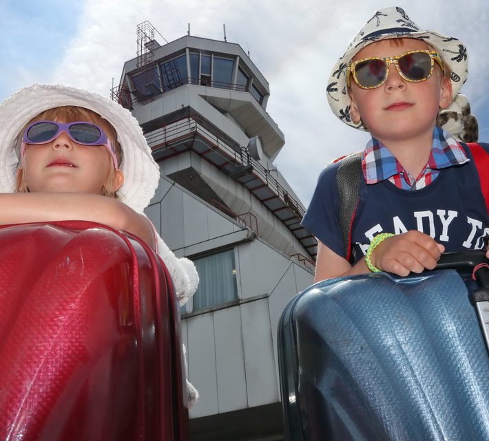 Geschwisterpaar mit Koffer, Sonnenbrille und Hut vor Tower | © Linz Airport