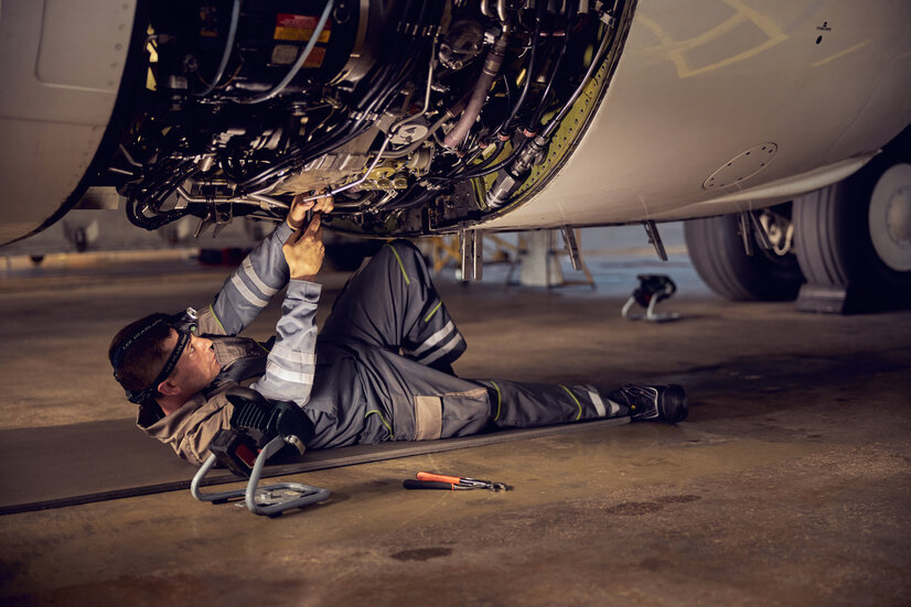 Fluggerätemechaniker am Boden liegend beim Warten eines Triebwerks | © Envato Elements