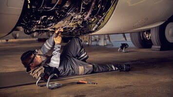 Fluggerätemechaniker am Boden liegend beim Warten eines Triebwerks | © Envato Elements