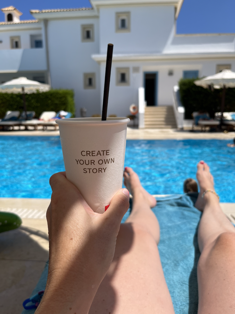 Touristin hält Kaffeebecher mit "Create your own story" auf Liege vor Pool in der Hand | © Linz Airport