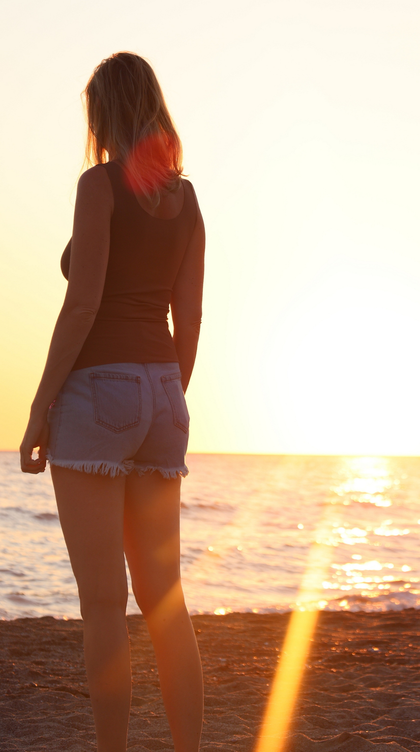 Frau mit ärmellosem T-Shirt und Jeansshorts im Sonnenuntergang vor Meer | © Linz Airport