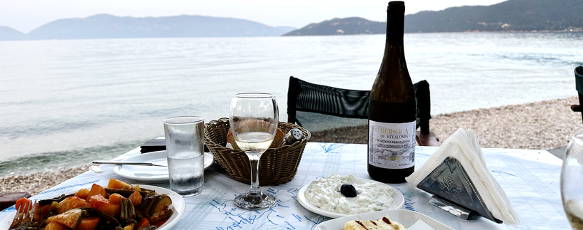 Tisch am Strand von Kefalonia gedeckt mit Tzatziki, gegrillten Käse und Gemüse und Wein | © Linz Airport