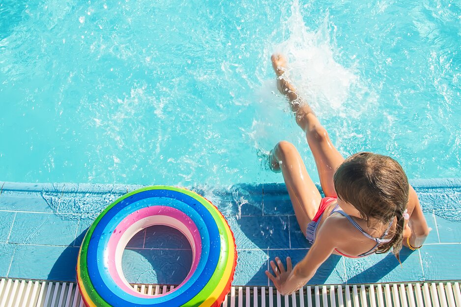 Mädchen mit buntem Schwimmreifen planscht am Poolrand | © Envato Elements