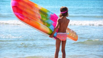Kleines Mädchen mit bunter Luftmatratze am Strand | © Envato Elements