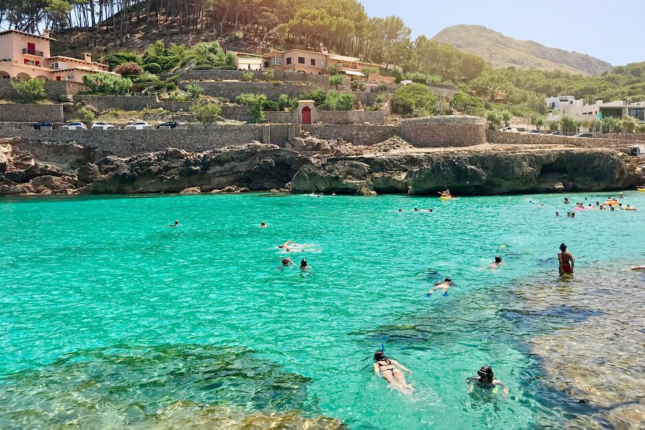 Türkisfarbene Meeresbucht und badende Touristen mit mallorquinischen Häusern im Hintergrund | © Envato Elements