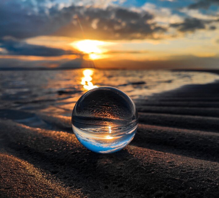 Glaskugel am Strand in der sich der Sonnenuntergang spiegelt | © unsplash