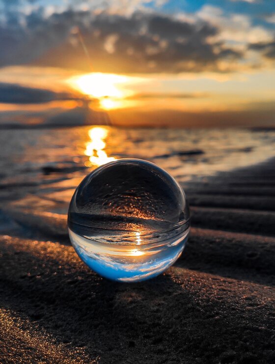 Glaskugel am Strand in der sich der Sonnenuntergang spiegelt | © unsplash