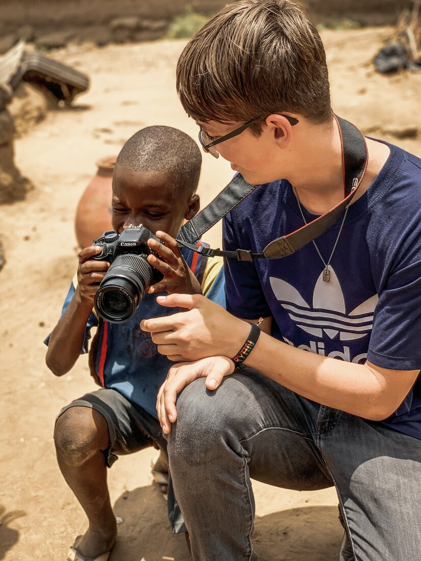Junger Tourist zeigt afrikanischem Kind seine Kamera | © Unsplash