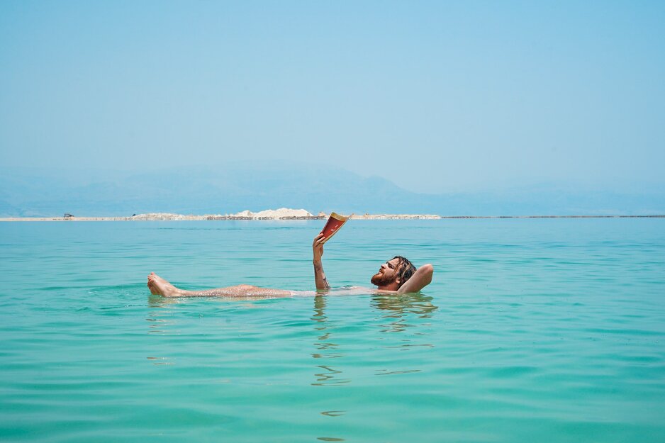 Mann mit Comic liegt auf dem Rücken schwimmend in Salzsee | © Toa Heftiba Unsplash