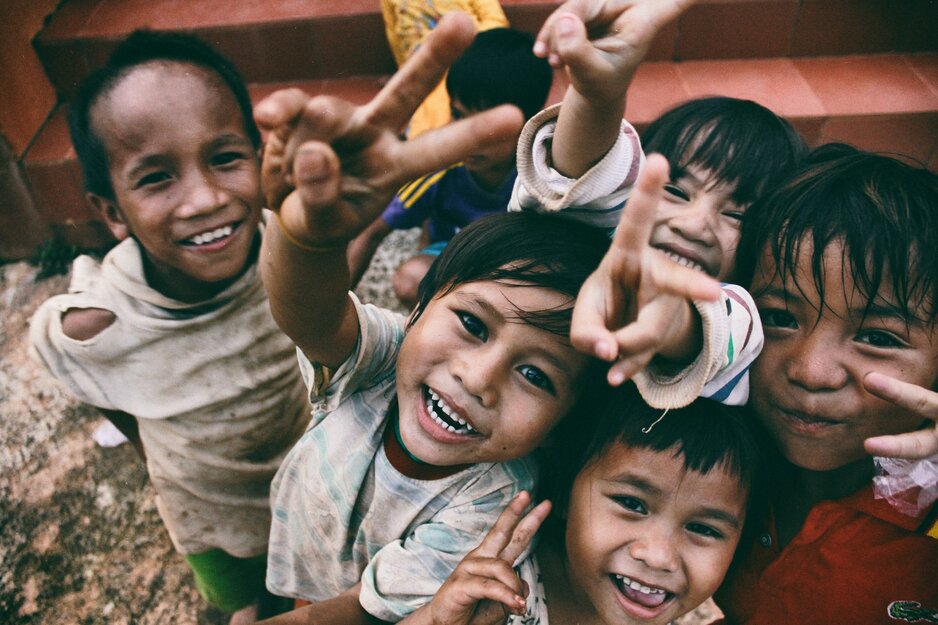 Kinder lachen in die Kamera und zeigen das Victory-Zeichen | © AEaTUnvneik Unsplash