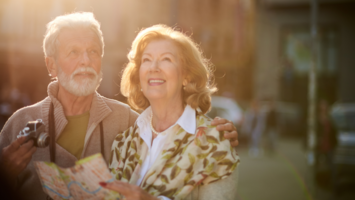 Älteres Paar mit Kamera und Stadtführer lächelt glücklich im Sonnenschein | © Canvas