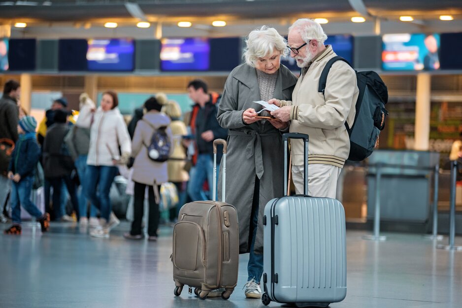 Älteres Paar mit Koffern betrachtet in der Abfllughalle konzentriert Flugtickets | © Adobe Stock 