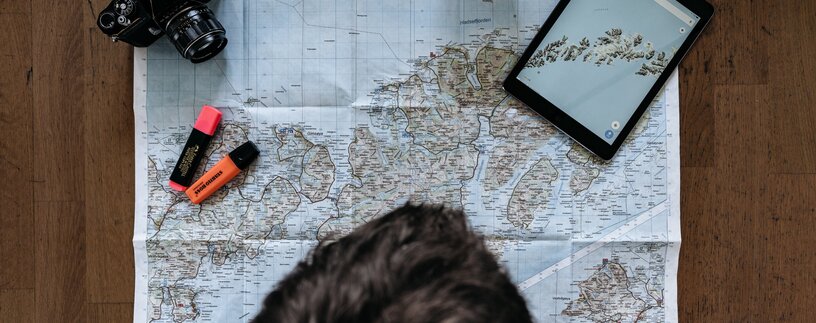 Person betrachtet Landkarte, daneben liegt iPad und Kamera | © Unsplash