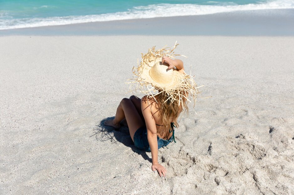 Frau im Bikini und Sonnenhut sitzend am Sandstrand | © Envato Elements