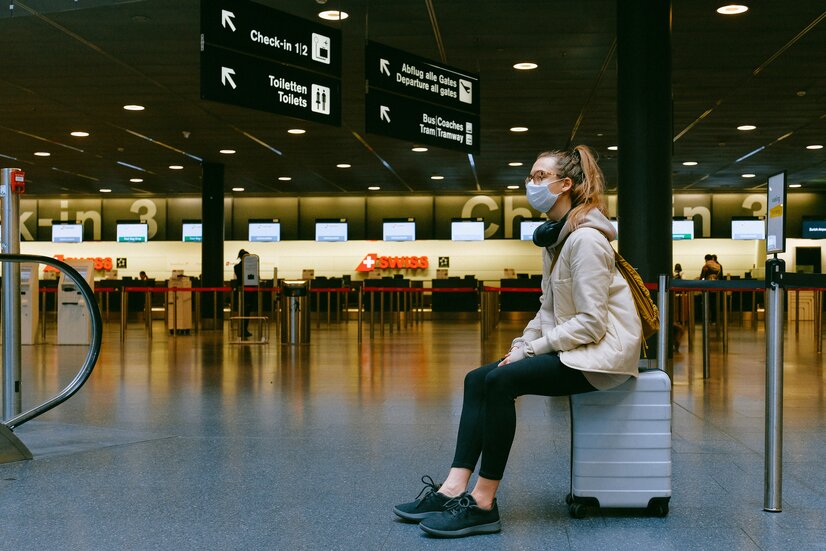 Junge Frau am Koffer sitzend, wartend in der Abflughalle | © Pexels