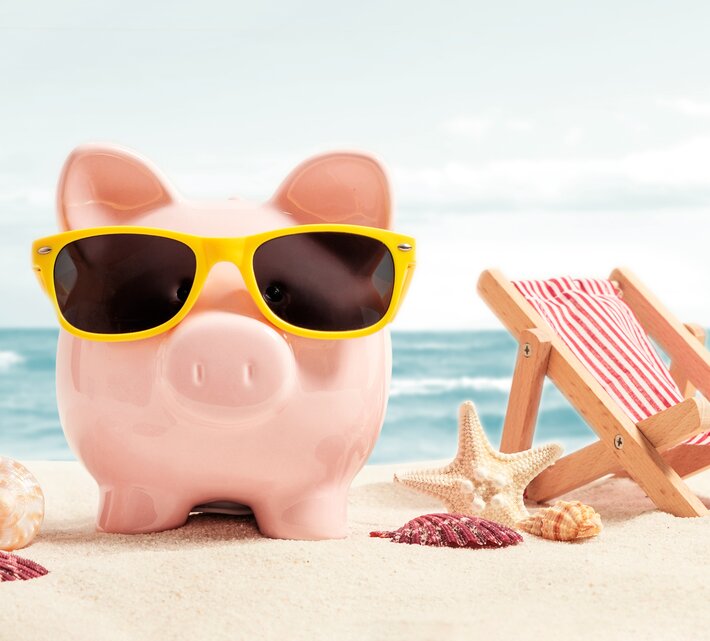 Pinkes Sparschwein mit gelber Sonnenbrille am Strand | © Adobe Stock