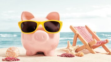 Pinkes Sparschwein mit gelber Sonnenbrille am Strand | © Adobe Stock
