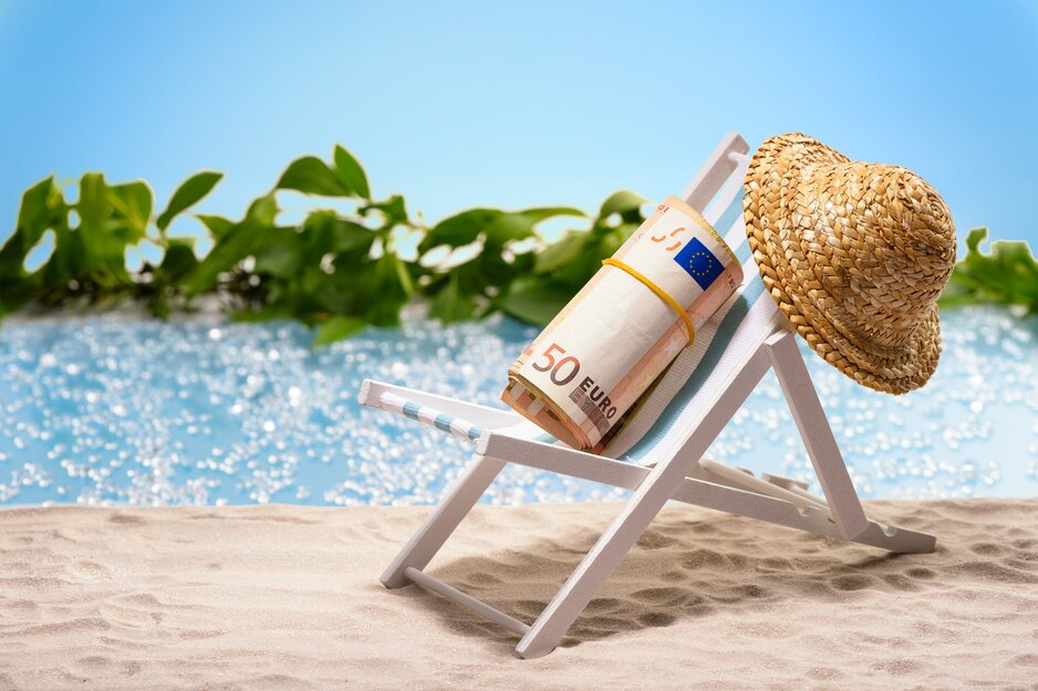 Kleiner Liegestuhls mit Sonnenhut und Geldrolle am Strand | © Adobe Stock