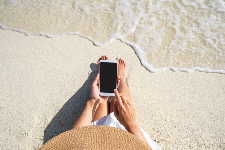 Junge Frau benützt Handy am Strand | © Adobe Stock
