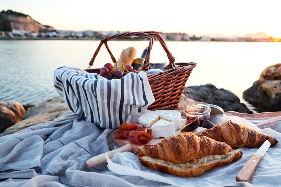 Befüllter Picknickkorb und frische Croissants auf Picknickdecke am Strand | © Adobe Stock