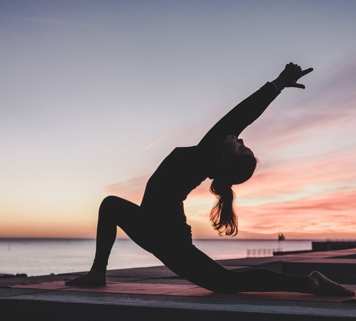 Silhouette einer Frau bei Yogaübungen am Strand | © Photo by <a href="https://unsplash.com/@kikekiks?utm_source=unsplash&utm_medium=referral&utm_content=creditCopyText">kike vega</a> on <a href="https://unsplash.com/?utm_source=unsplash&utm_medium=referral&utm_content=creditCopyText">Unsplash</a>   