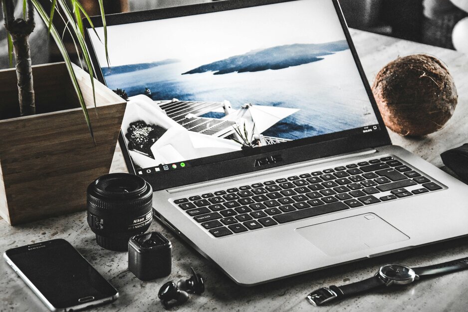 Geöffneter Laptop mit Urlaubsbild und Kameraobjektive auf Tisch | © Unsplash