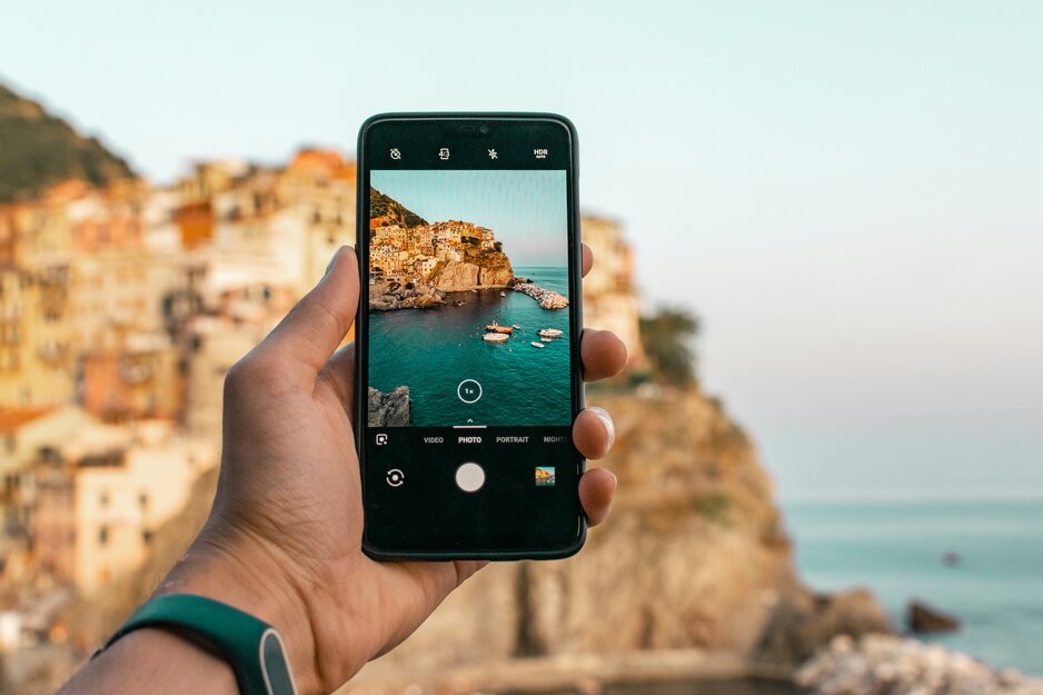 Mann hält Handy und macht Foto von Küstenstädtchen | © Unsplash