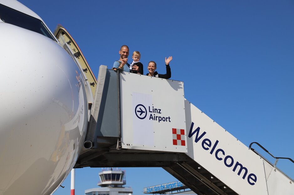 Winkende Familie mit Baby beim Einsteigen auf Fluggasttreppe | © Linz Airport