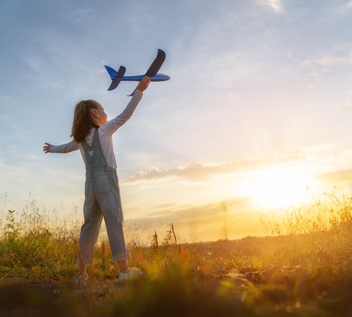 Kleines Mädchen mit Spielzeugflugzeug in der Hand im Sonnenschein auf Wiese | © Envato Elements