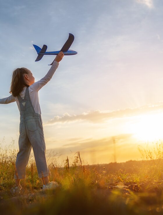 Kleines Mädchen mit Spielzeugflugzeug in der Hand im Sonnenschein auf Wiese | © Envato Elements