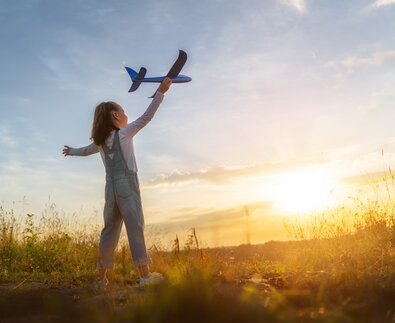 Kleines Mädchen mit Spielzeugflugzeug in der Hand im Sonnenschein auf Wiese | © Envato Elements