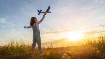 Kleines Mädchen mit Spielzeugflugzeug in der Hand im Sonnenschein auf Wiese | © Envato Elements
