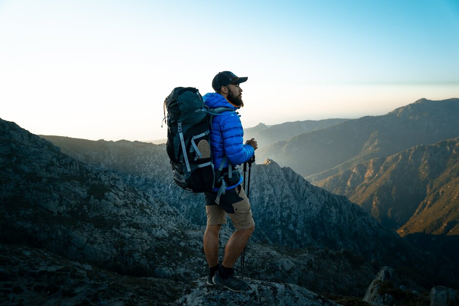 Wanderer mit großem Rucksack blickt auf Bergkette | © Lucas Favre Unsplash