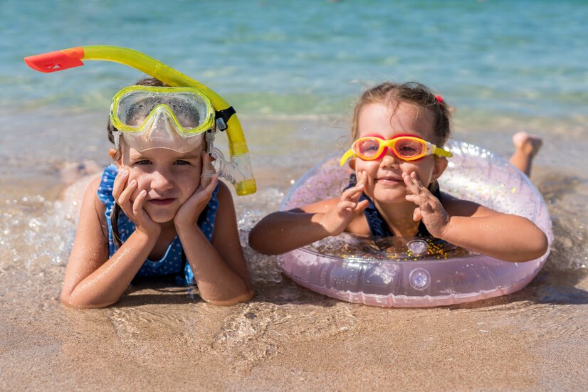 Kinder mit Taucherbrille und Schnorchel liegen im Sandstrand | © Envato